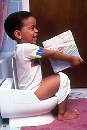 child sitting on a child's potty smiling and holding a book