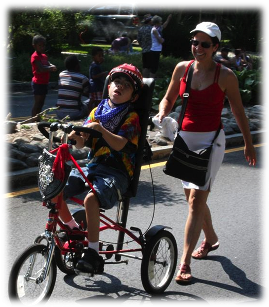 Mother following son who is riding an adaptive tricycle