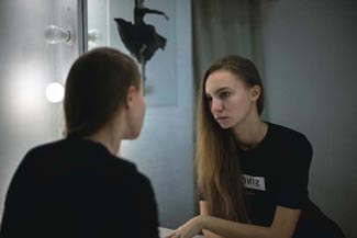 Teen girl looks unhappy in a bathroom mirror. Warning signs of eating disorders are numerous