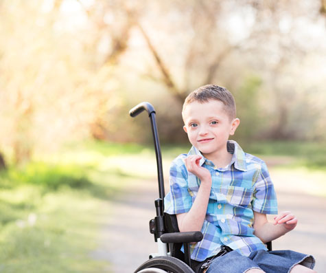 Grade-school boy with global developmental delay in wheelchair outside on winding path